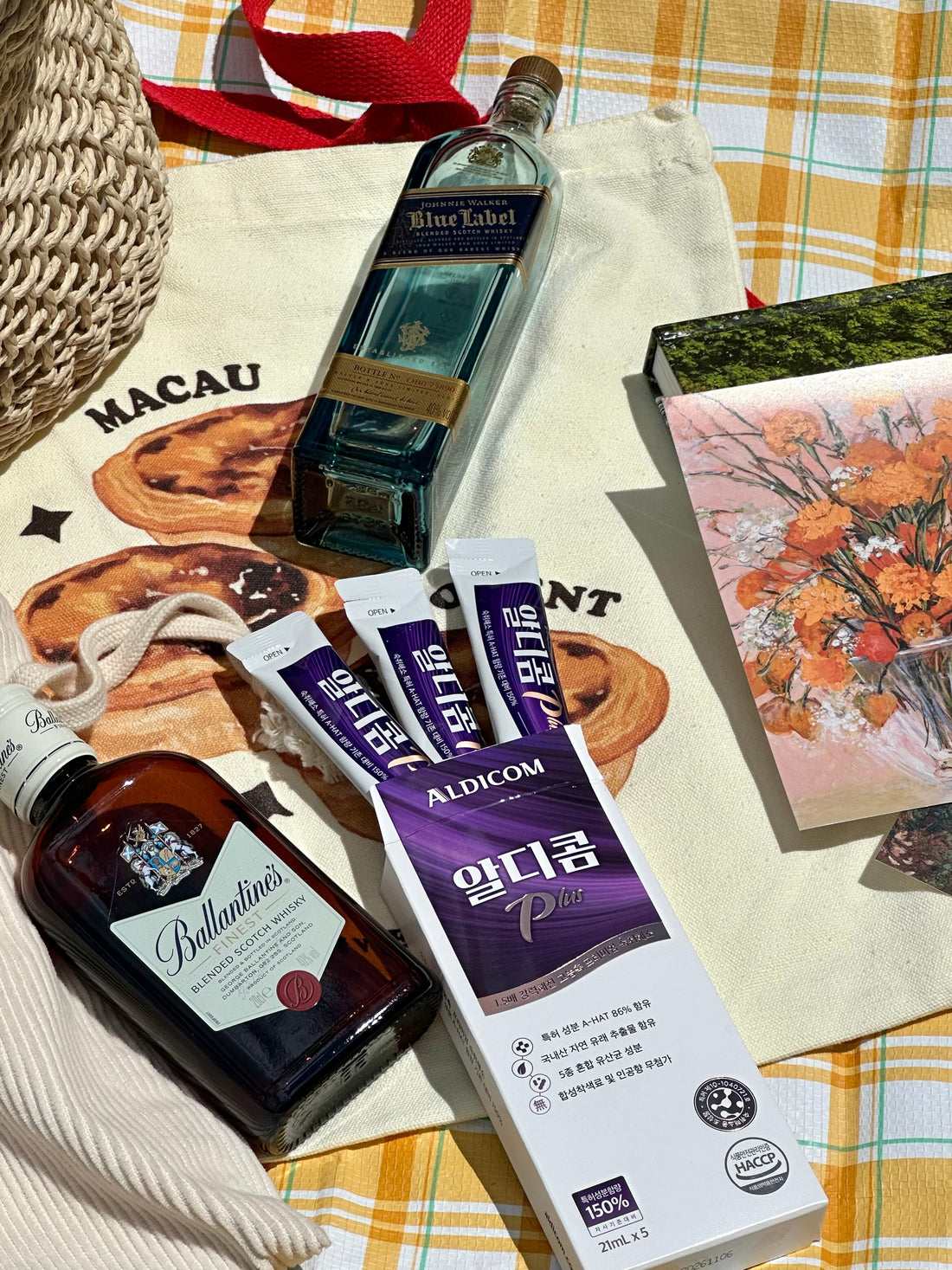"Flat lay of Aldicom Plus hangover relief sticks alongside premium whiskey bottles on a picnic setup—highlighting Aldicom as the smart companion for luxury drinking occasions."