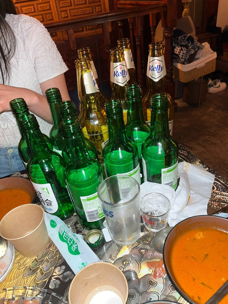 Korean Soju alcohol drinking. Table cluttered with empty soju and beer bottles after a heavy night out—ideal scenario for using Aldicom hangover relief for fast recovery.
