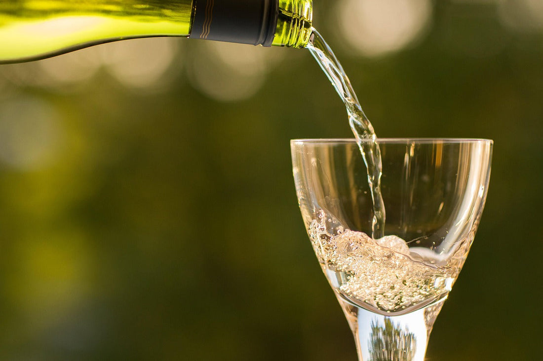"White wine being poured into a clear glass outdoors—capturing the start of a relaxing drink, where Aldicom can help prevent hangover symptoms before they begin."