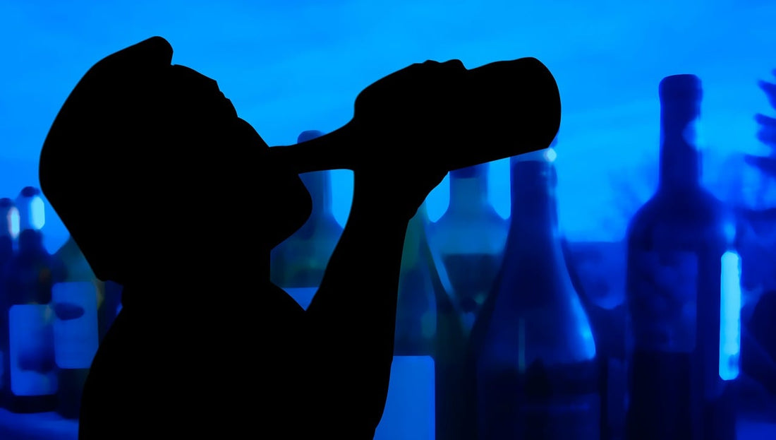 Silhouette of a person drinking from a bottle with various alcohol bottles in the background—symbolizing the lead-up to a hangover and the need for Aldicom’s preventive formula.