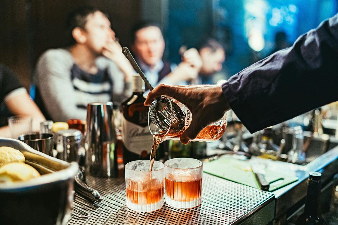 Bartender pouring cocktails at a lively bar with friends in the background—illustrating a night out where Aldicom hangover relief ensures a better tomorrow.