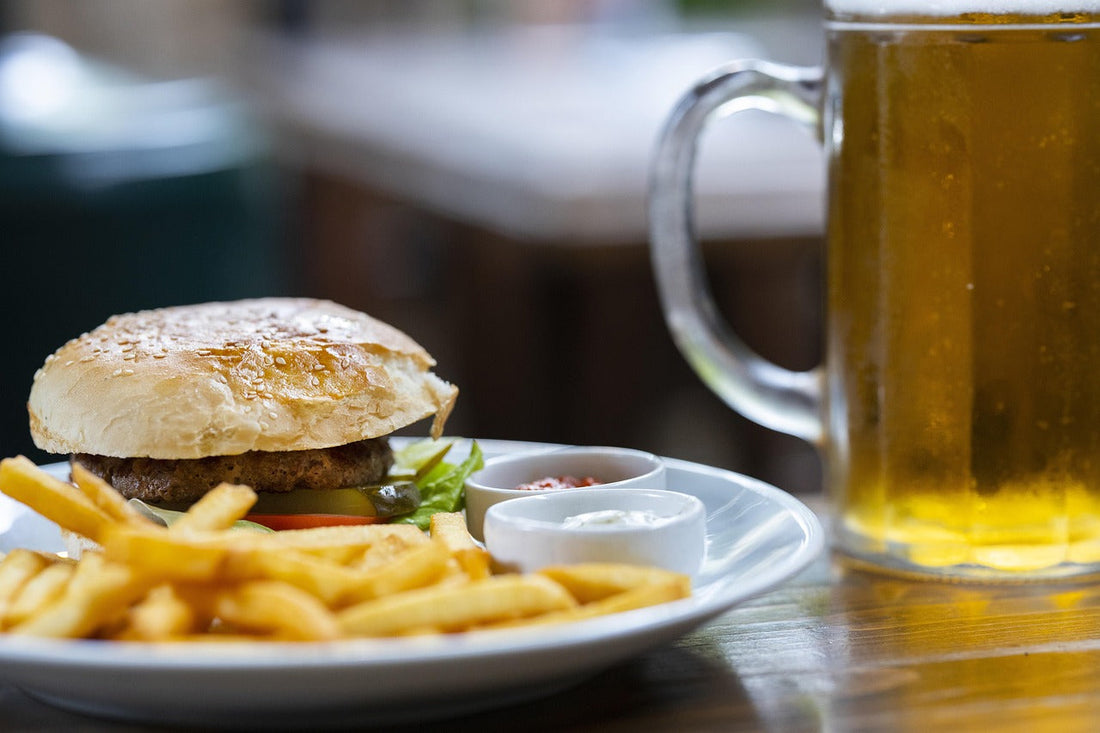 Close-up of a burger, fries, and a glass of beer on a table—classic hangover meal suggesting the need for Aldicom’s fast-acting recovery formula.