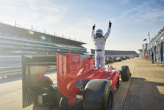 "Race car driver celebrating victory next to a red Formula 1 car on the track—capturing high-energy moments where Aldicom hangover relief keeps the celebration going strong.